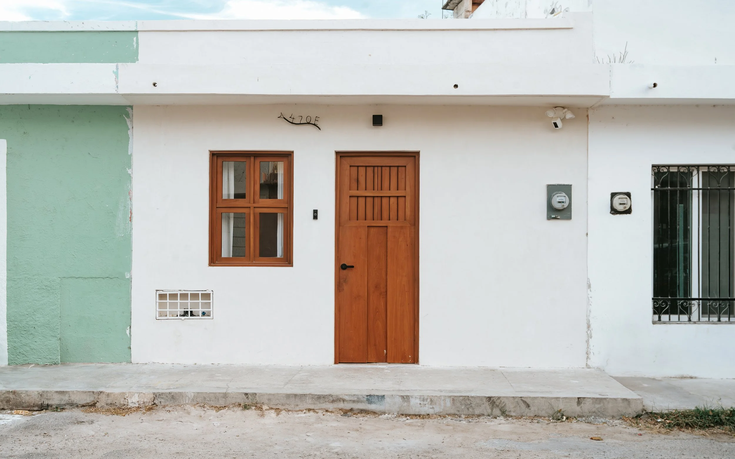 Front of a white building with a wooden door, window, and utility meters, with a green wall on the left side. colonial house merida, restoration project