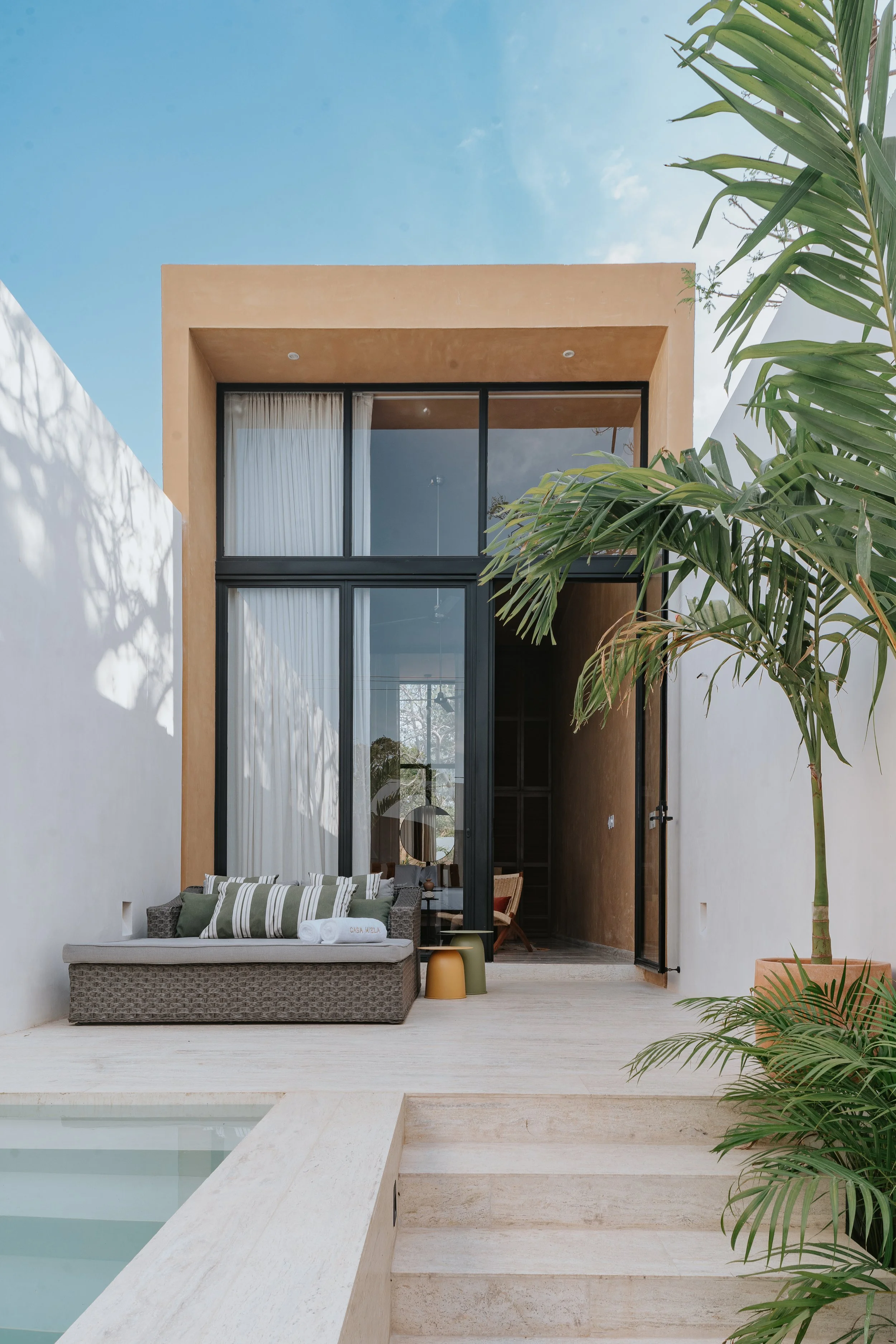 Modern house exterior with large glass doors, outdoor seating area, potted plants, and a swimming pool