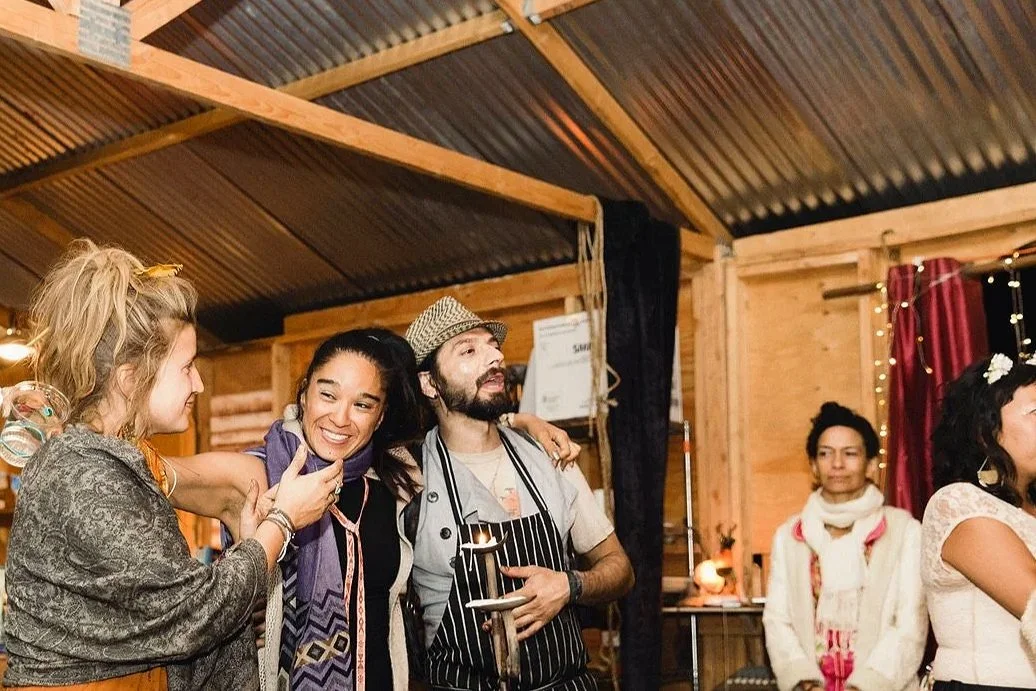 Group of people preparing food in a rustic wooden kitchen with shelves, utensils, and a large counter.