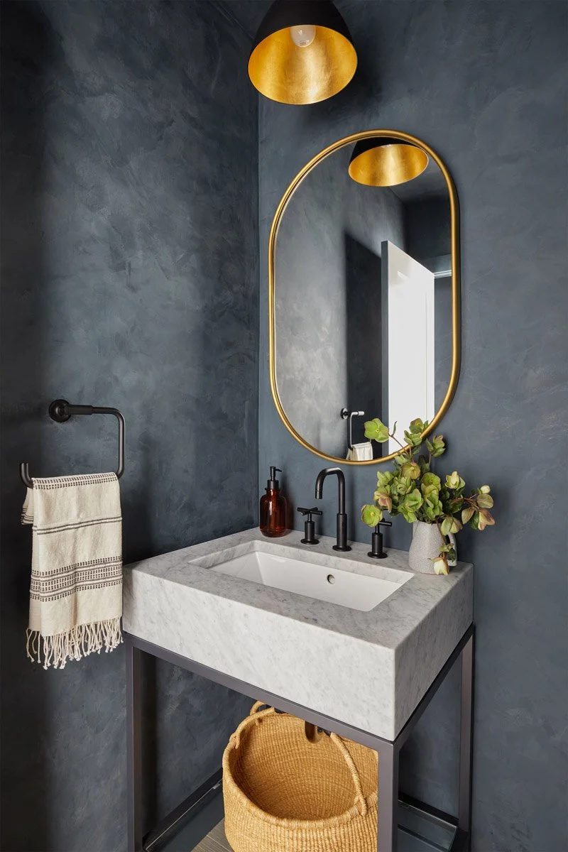 stone pedestal sink with oval brass mirror and black fixtures