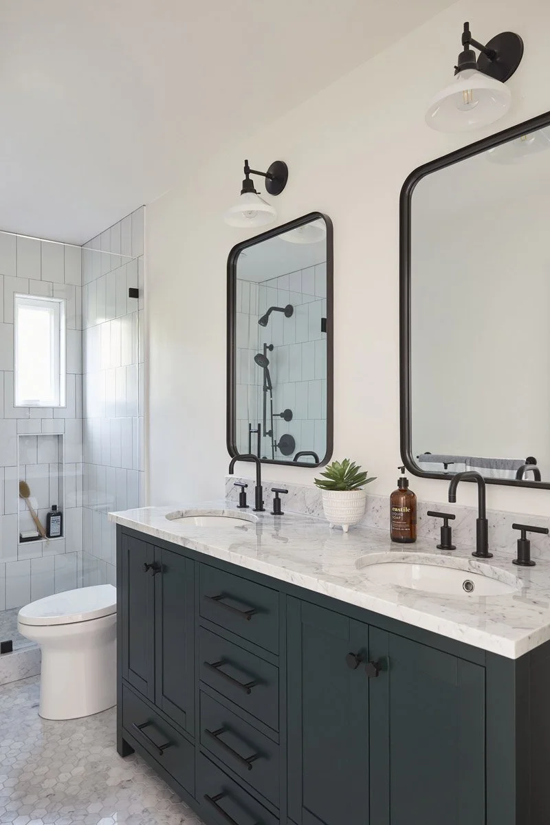 bathroom with dark green double vanity, black framed mirrors and marble countertop