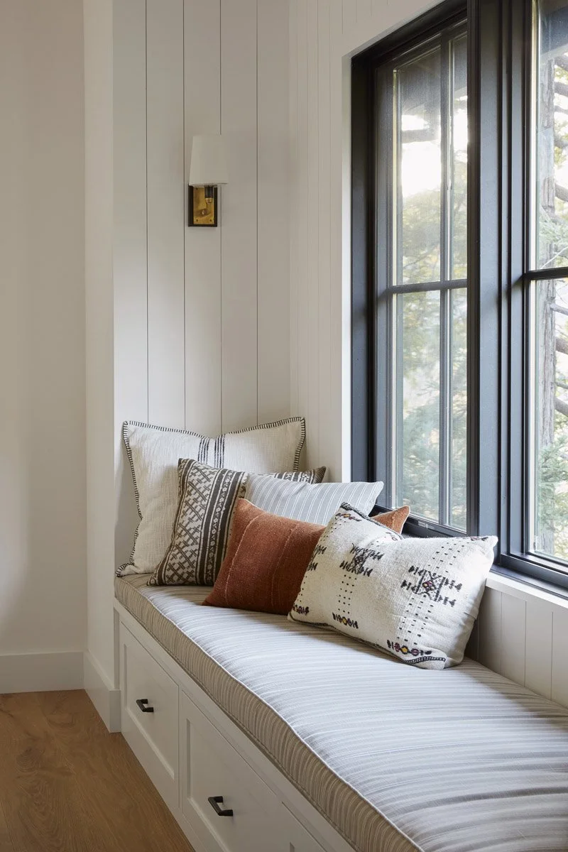 built-in window seat with patterned pillows and white panelled walls