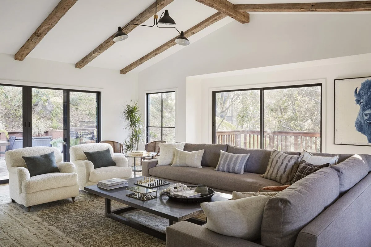 great room with grey sectional, cream armchairs and exposed wood beams