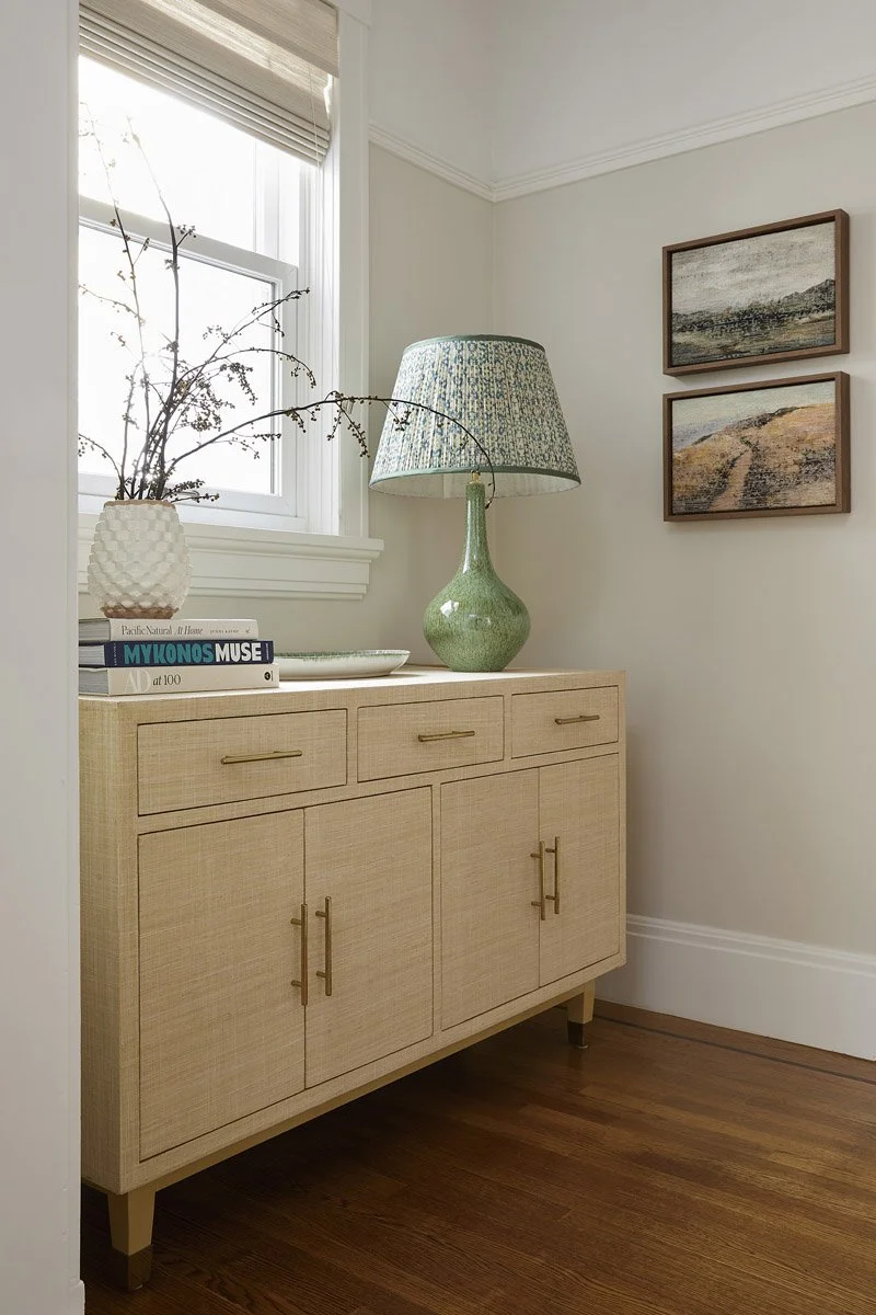 light wood sideboard with green ceramic lamp and framed landscape prints