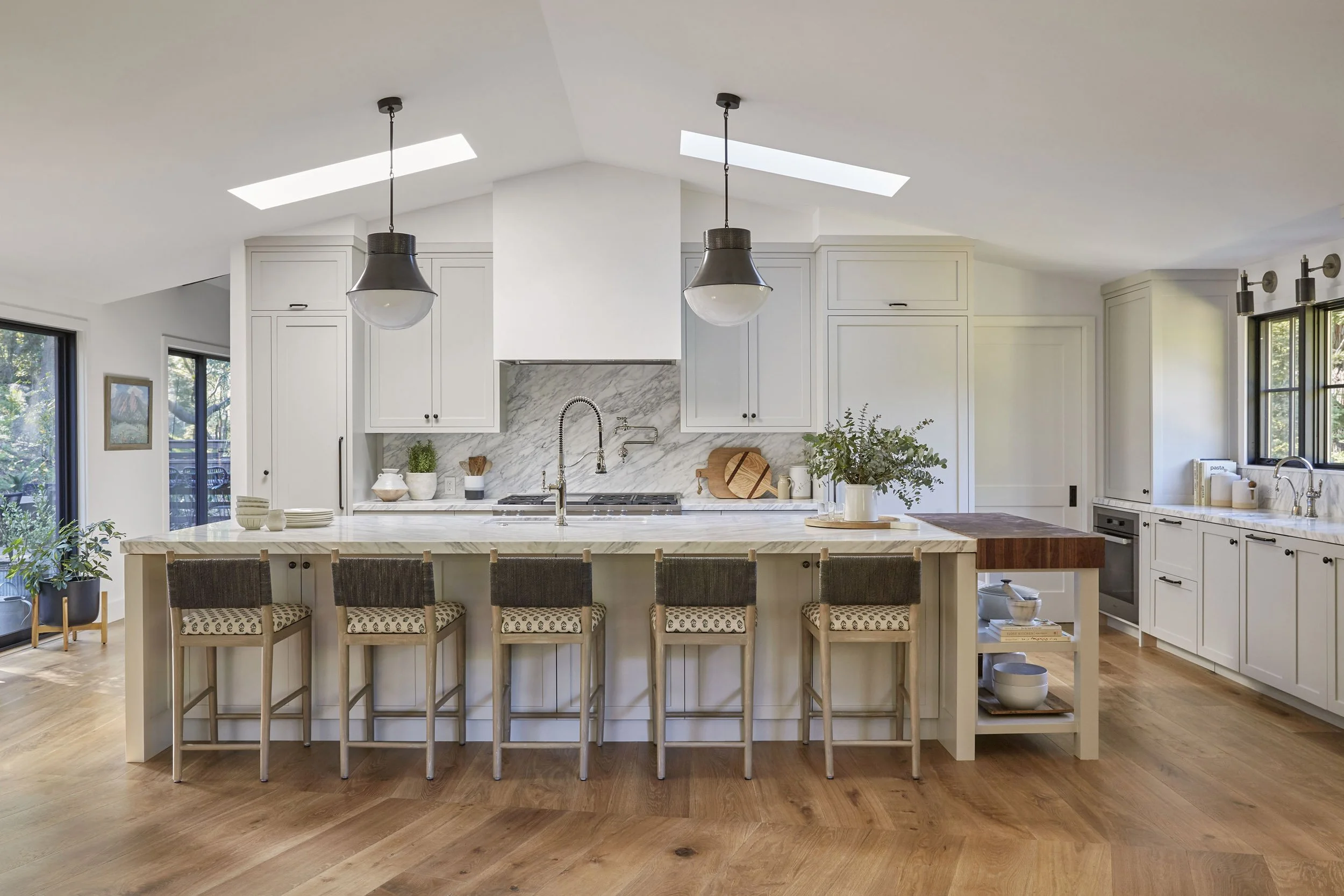 open kitchen with white oak island, woven counter stools and black pendant lights