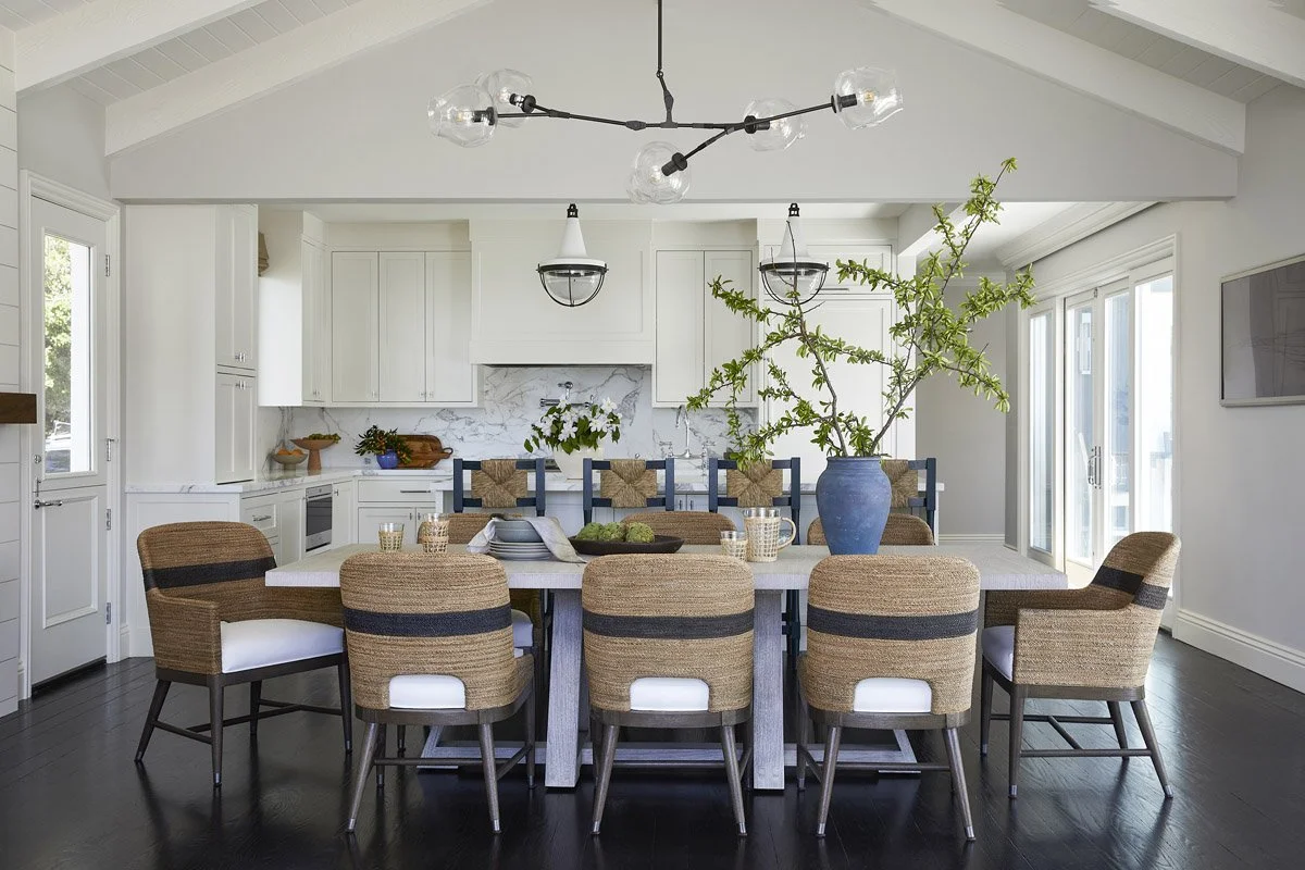 long dining table with woven chairs and green branches in a blue vase