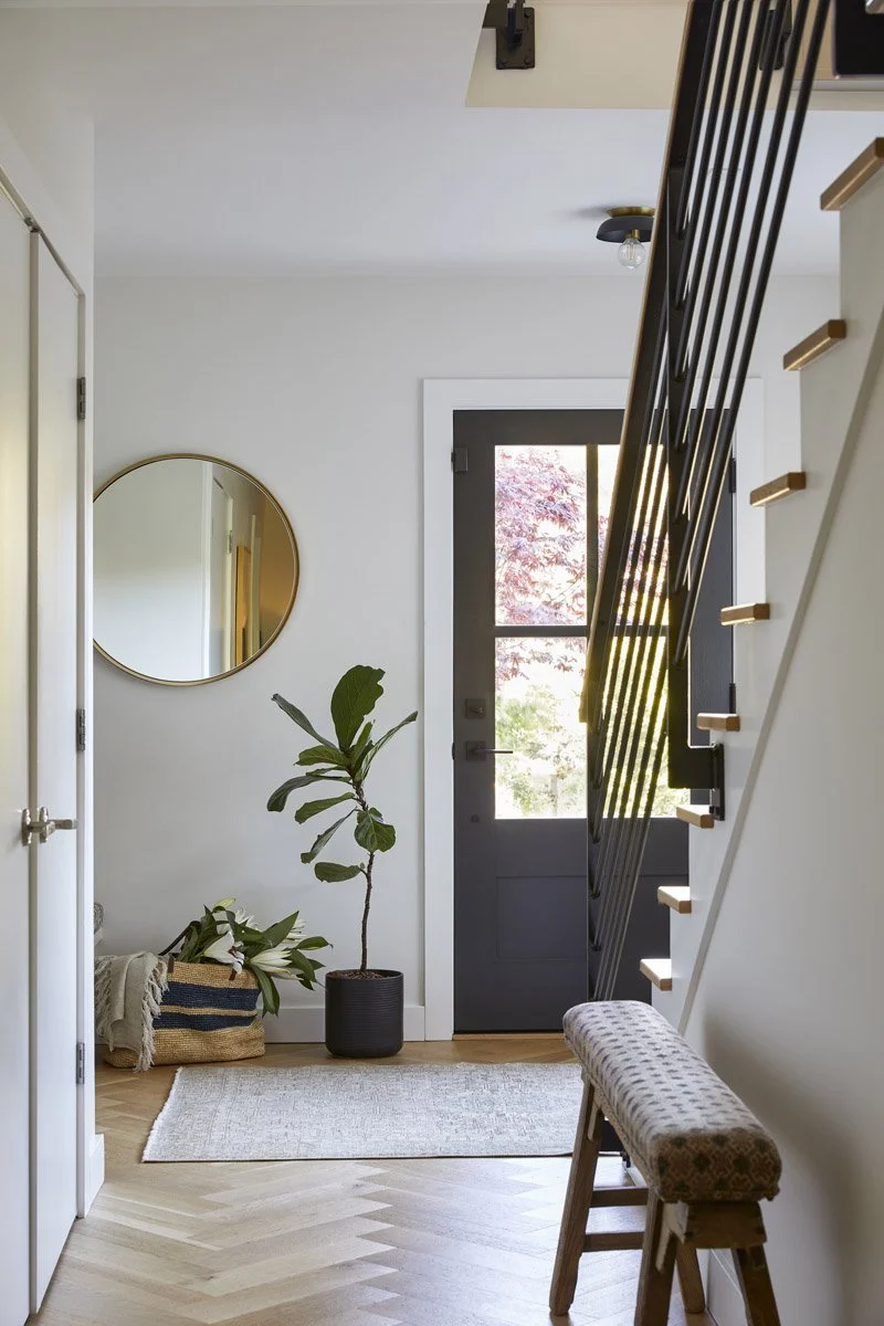 entryway with round mirror, black front door and open staircase