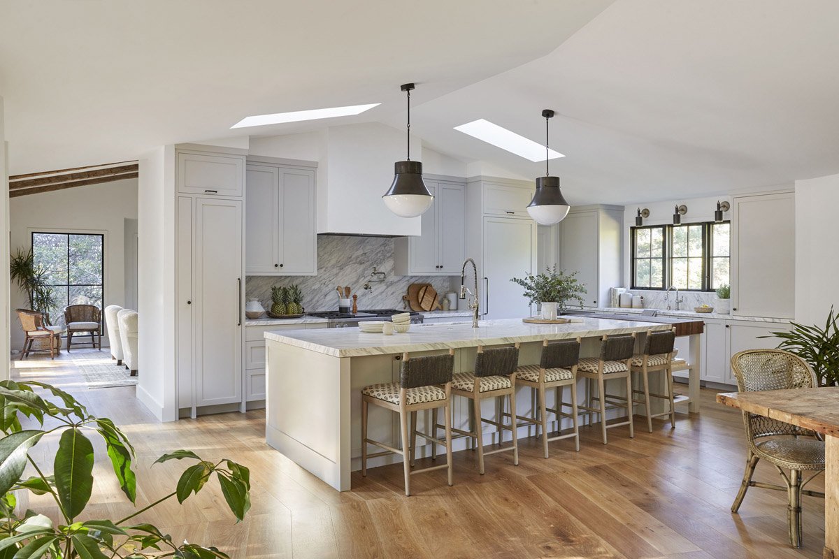 open kitchen with long marble island, woven counter stools and skylights
