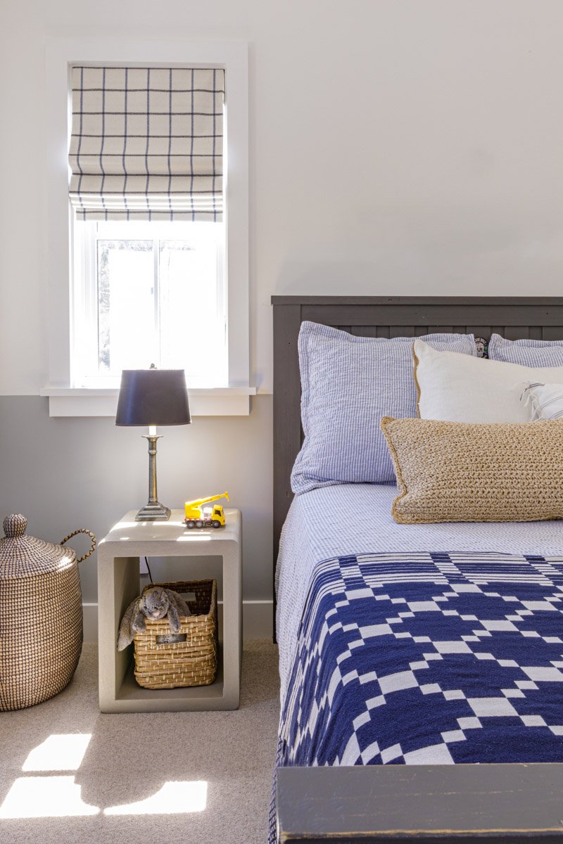 bedroom with navy patterned bedding, woven roman shade and wicker nightstand