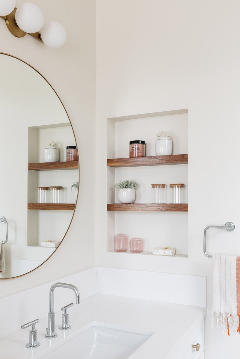bathroom with built-in wood niche shelves and round mirror