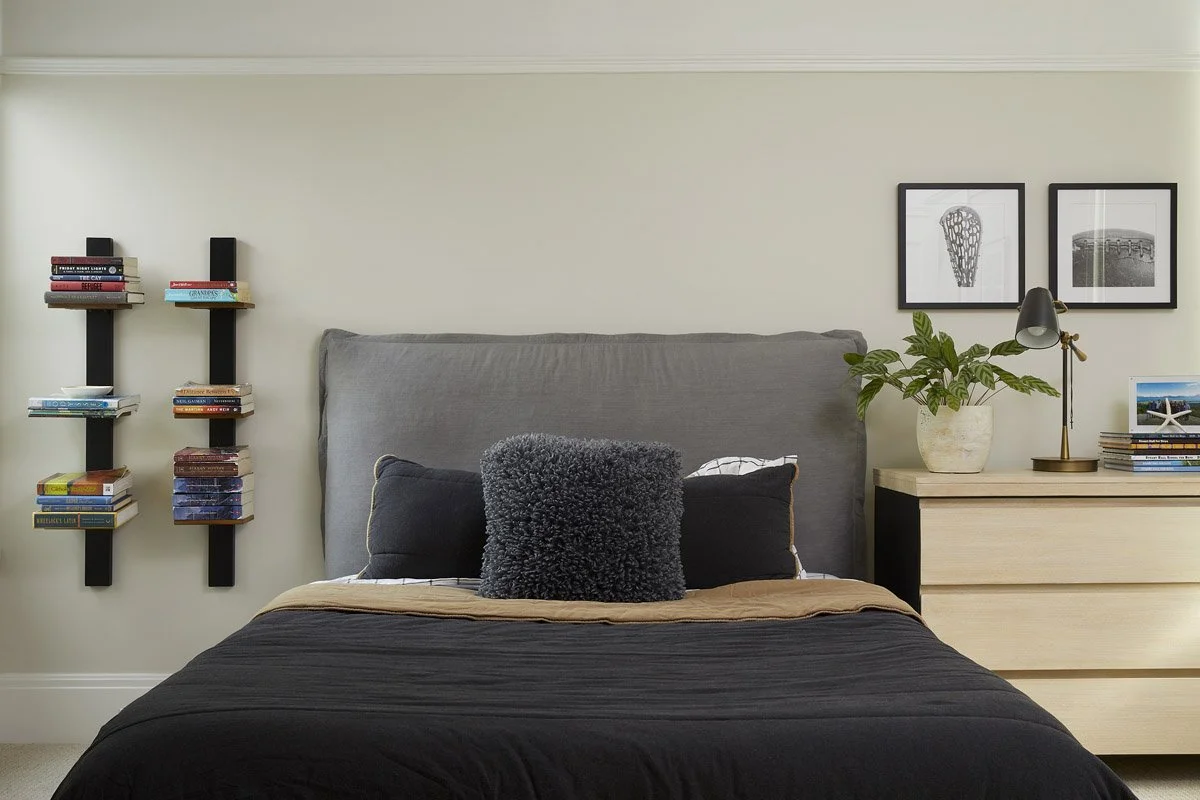 bedroom with charcoal upholstered bed, floating book shelves and framed prints