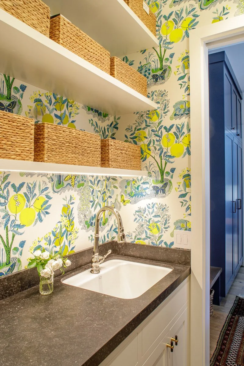 laundry sink with woven baskets on open shelves and lemon print wallpaper