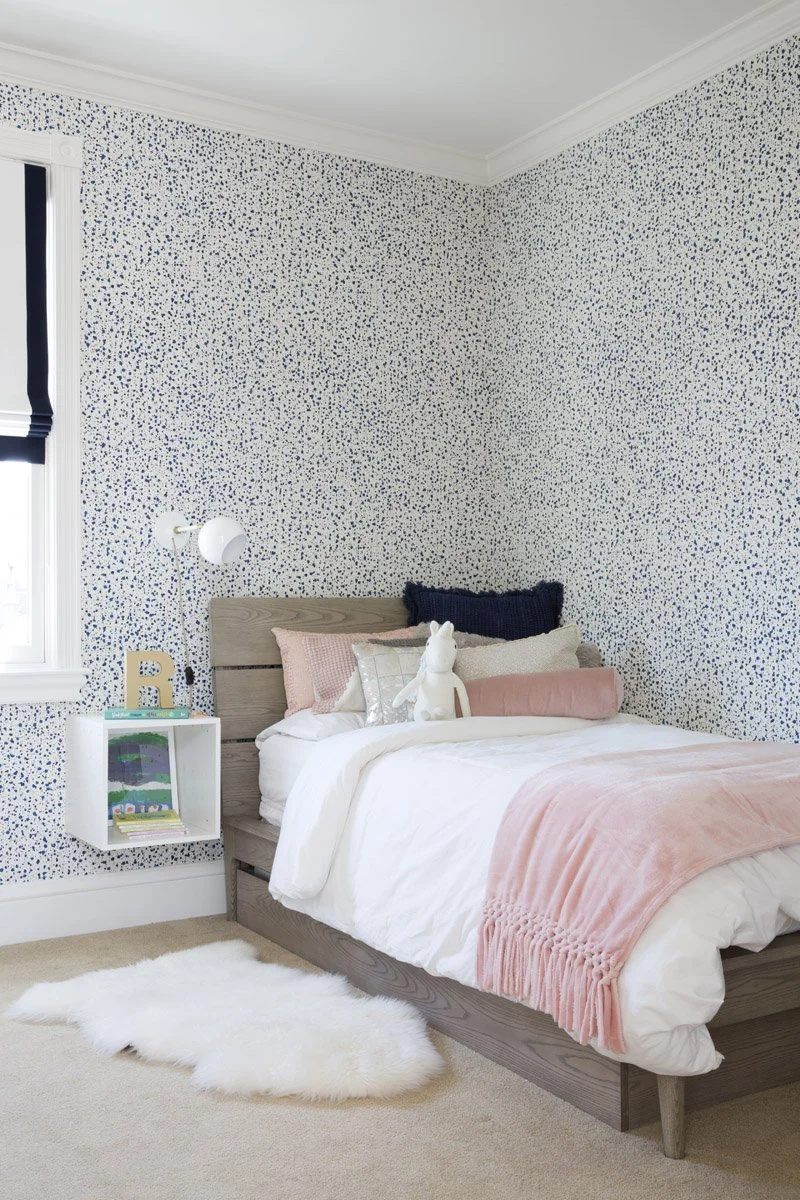 girls bedroom with speckled wallpaper, pink bedding and sheepskin rug