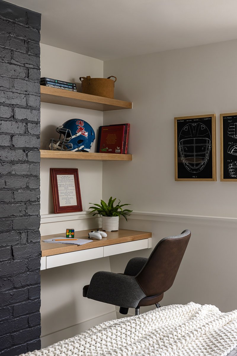 built-in desk with floating wood shelves beside a painted brick chimney