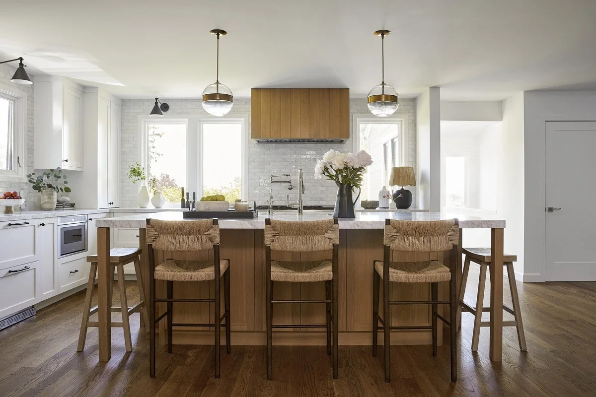 kitchen with white oak island, woven counter stools and brass pendant lights