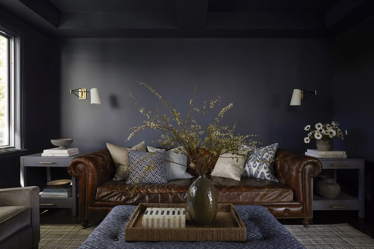 navy den with chesterfield sofa, upholstered ottoman and brass sconces