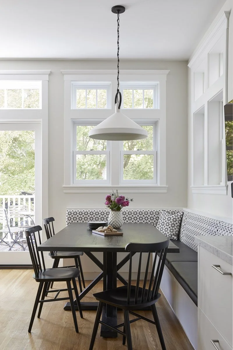 dining nook with black table and spindle chairs beneath tall windows