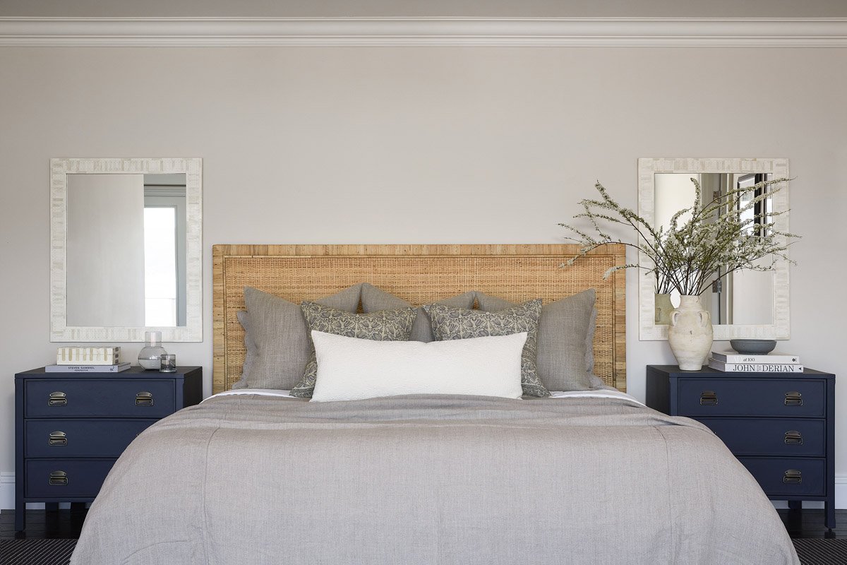 bedroom with woven headboard, navy nightstands and white linen bedding