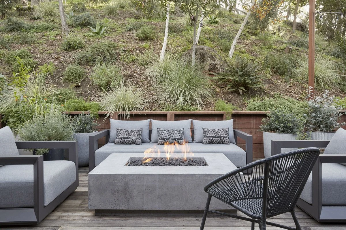 outdoor patio with concrete fire table, grey lounge seating and hillside garden