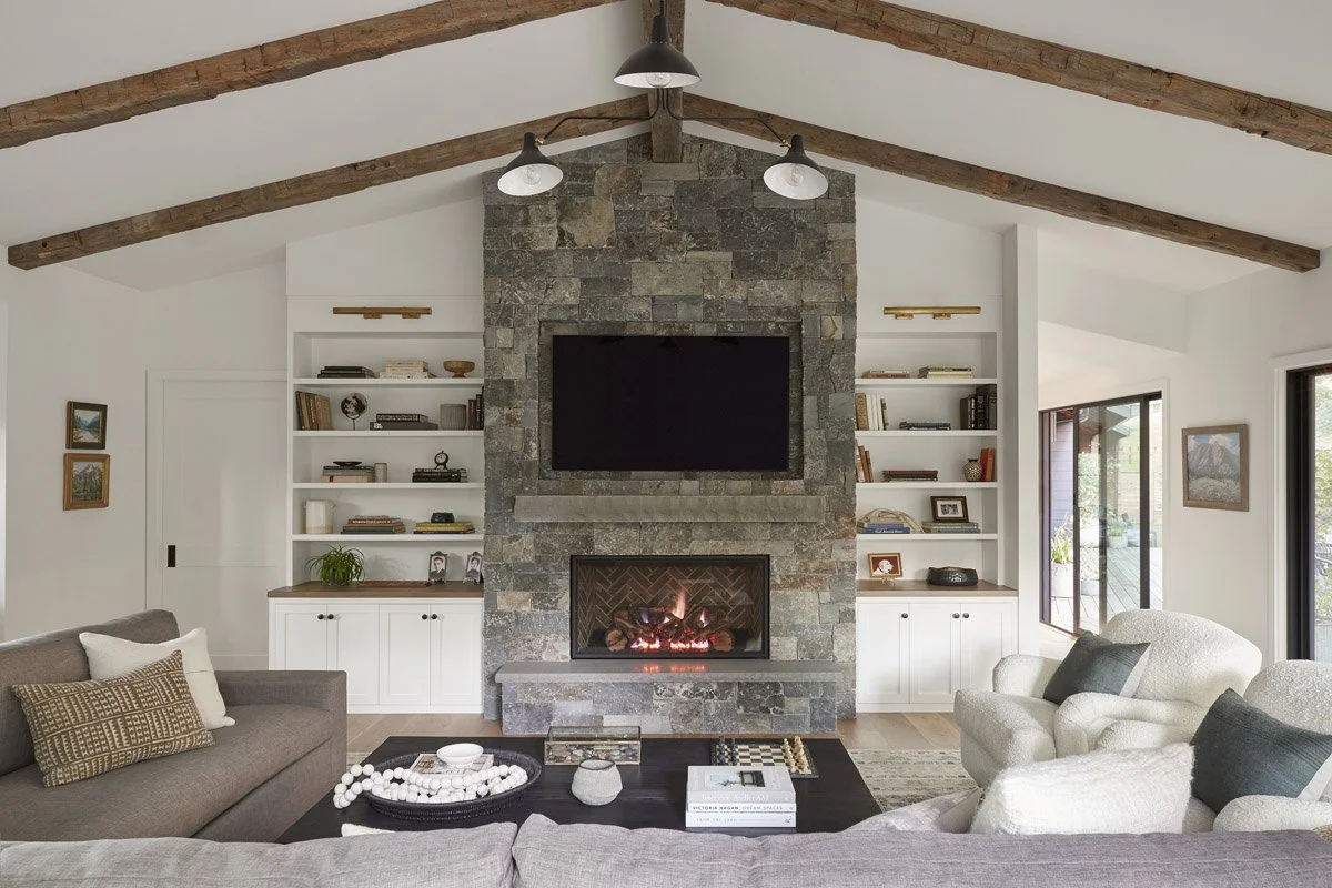 living room with stone fireplace, built-in shelving and vaulted wood beam ceiling