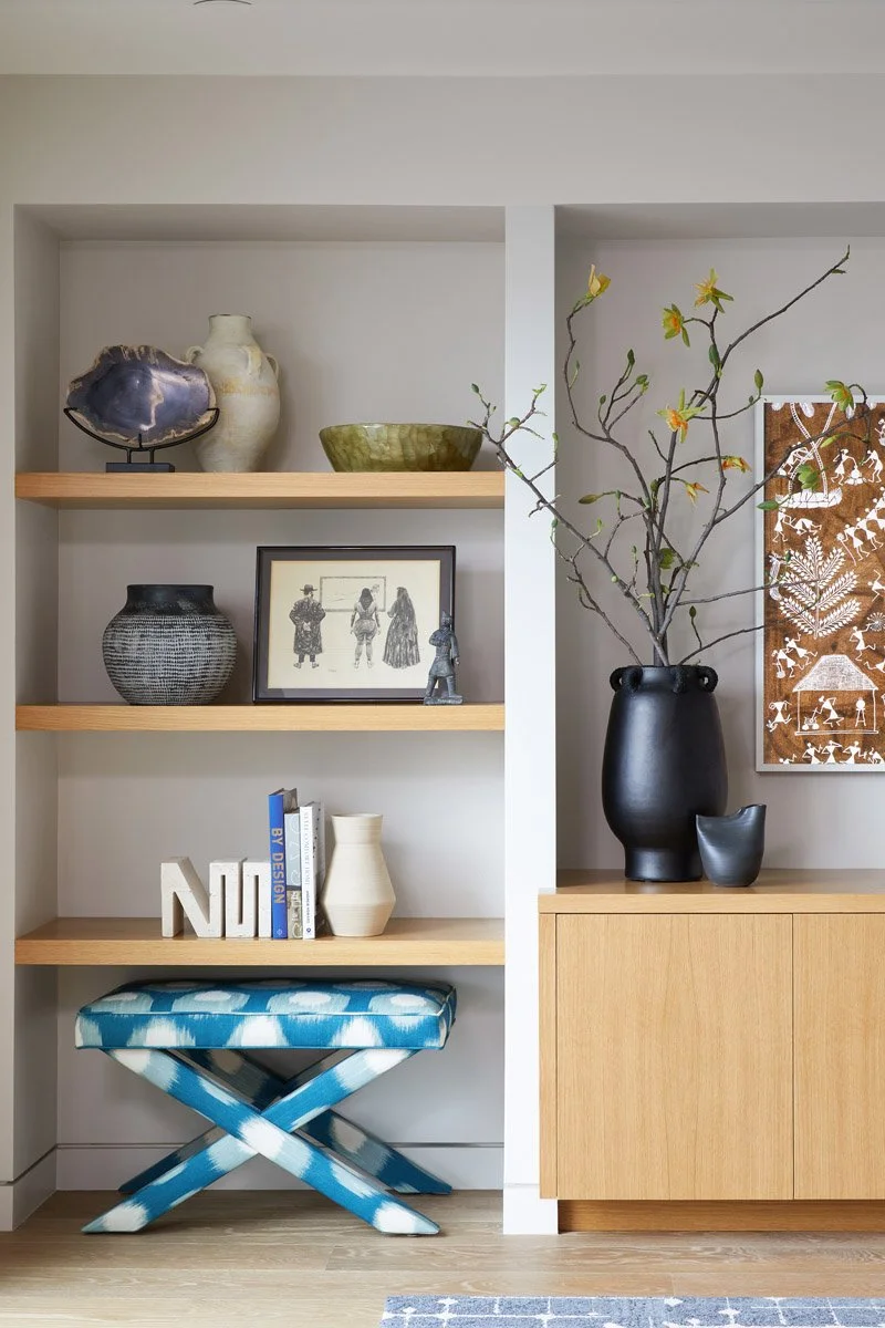built-in wood shelving styled with ceramics above a blue patterned bench