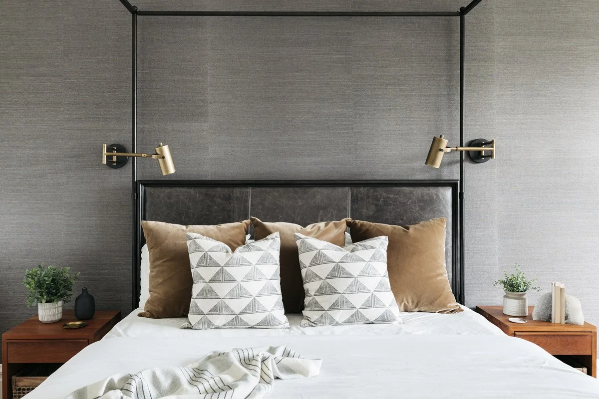 primary bedroom with leather headboard, brass swing-arm sconces and patterned pillows