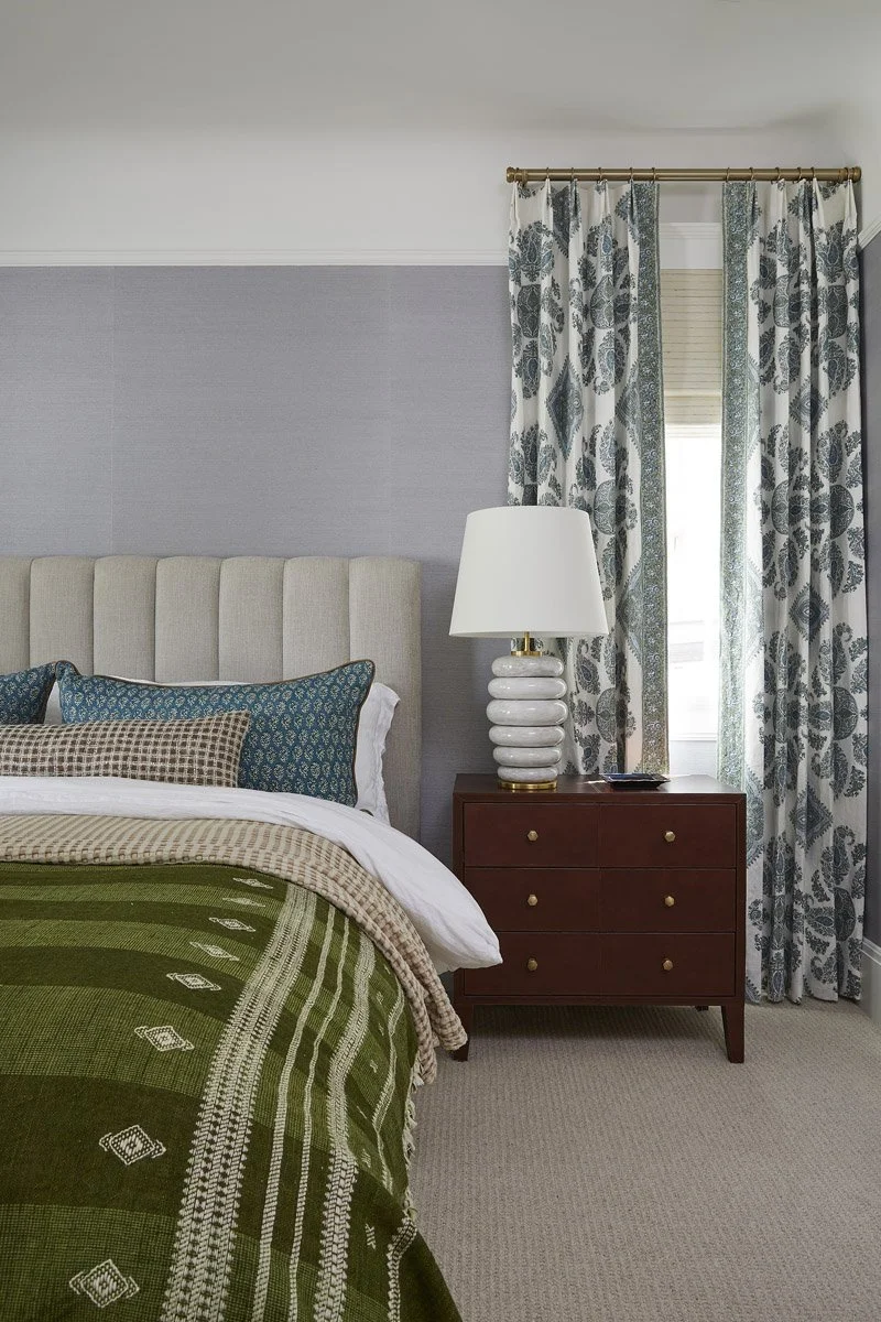 bed with green embroidered throw beside a dark wood nightstand