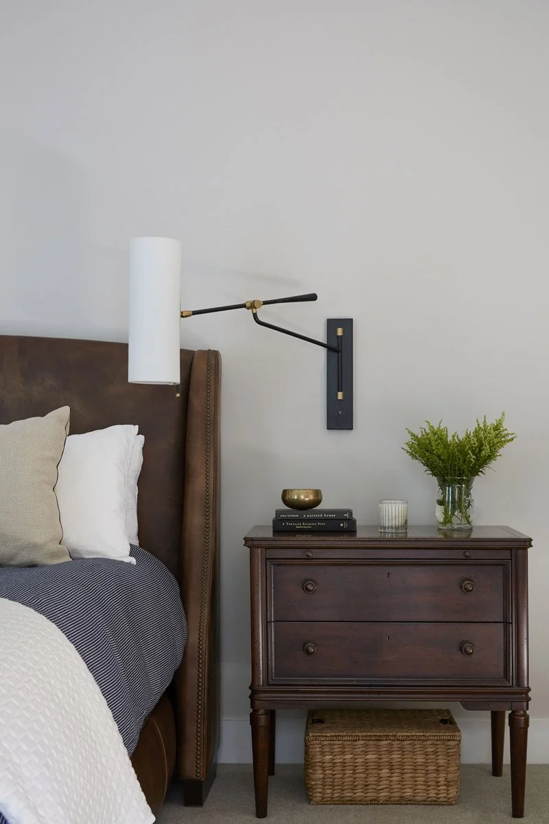 bedside detail with wall-mounted lamp and dark wood nightstand
