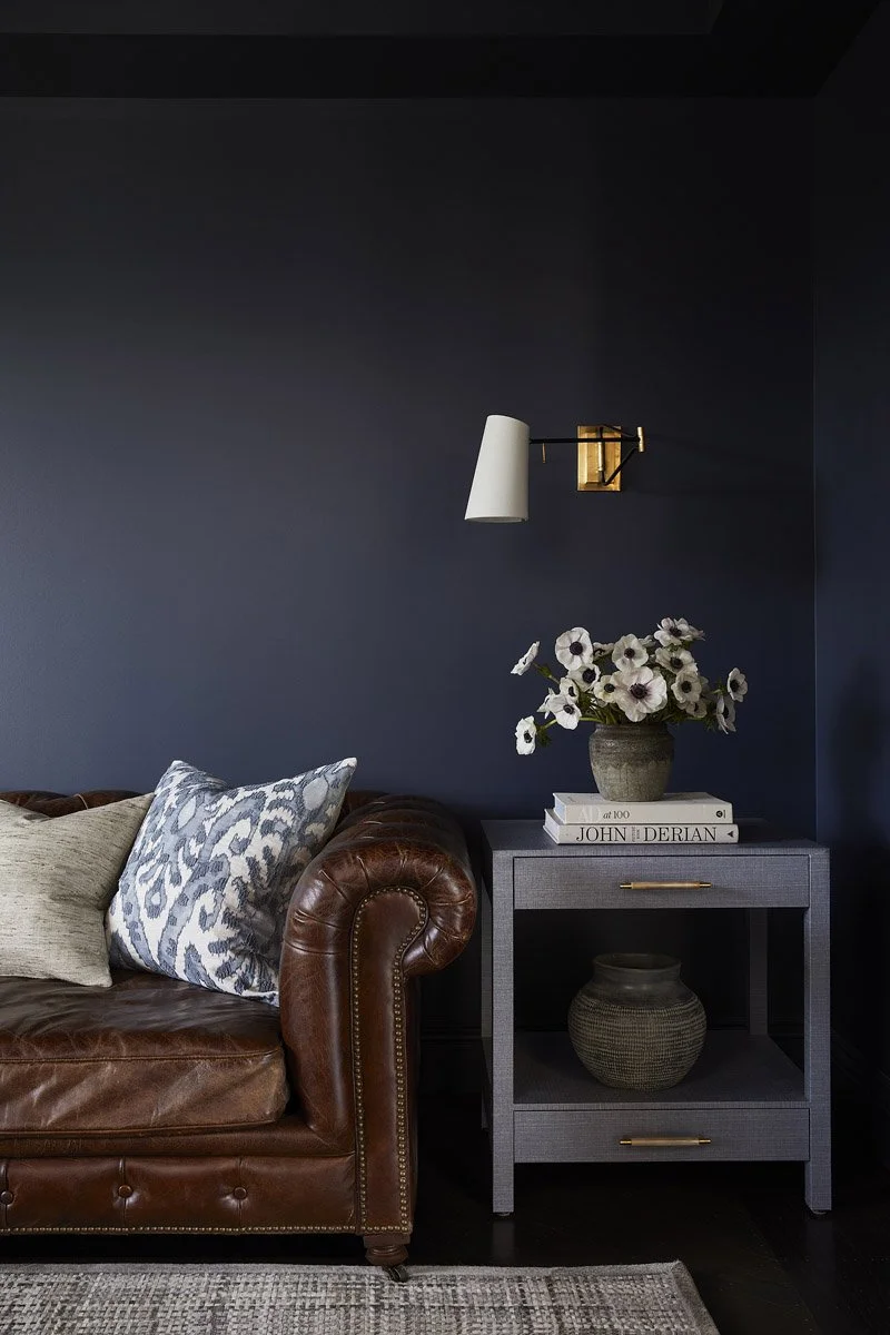 navy painted den with leather sofa, side table and brass wall sconce