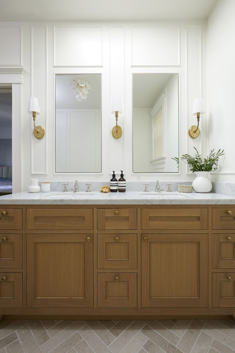 primary bathroom with wood double vanity, brass sconces and panelled walls