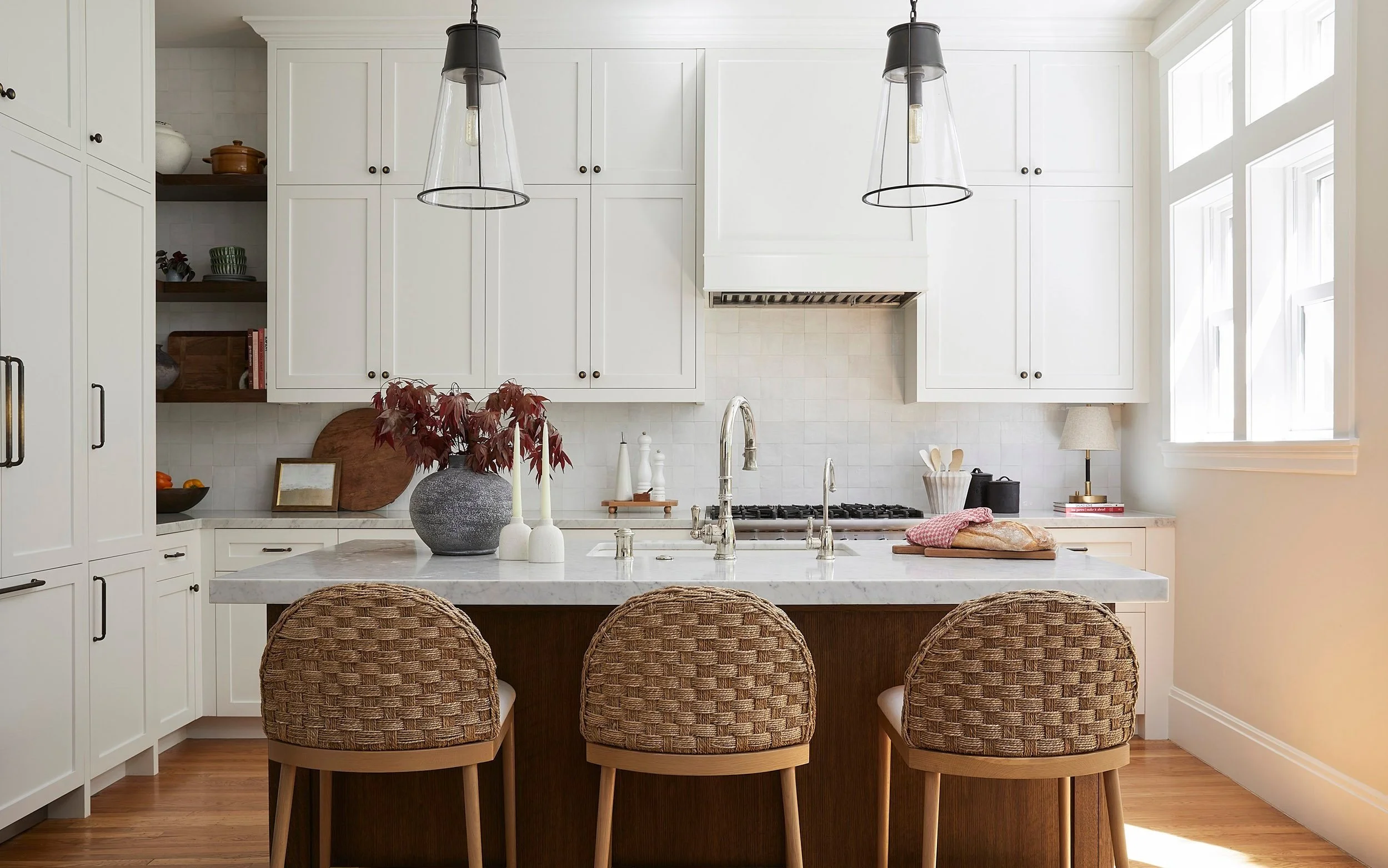 white kitchen with dark wood island and woven counter stools