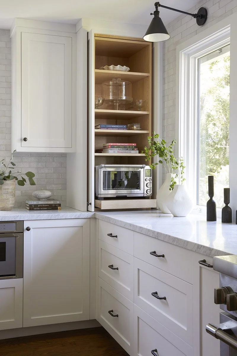 white kitchen corner with open appliance cabinet and black wall sconce