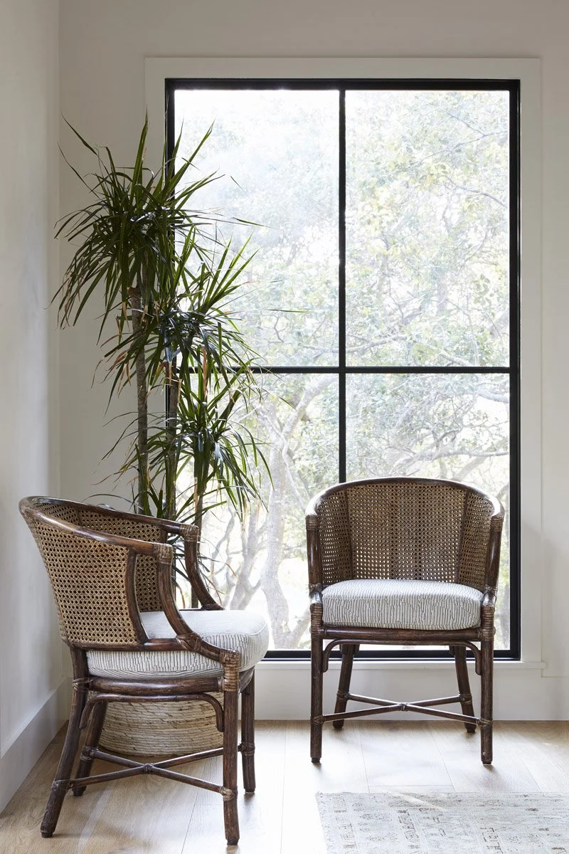 pair of rattan armchairs beside a large black-framed window