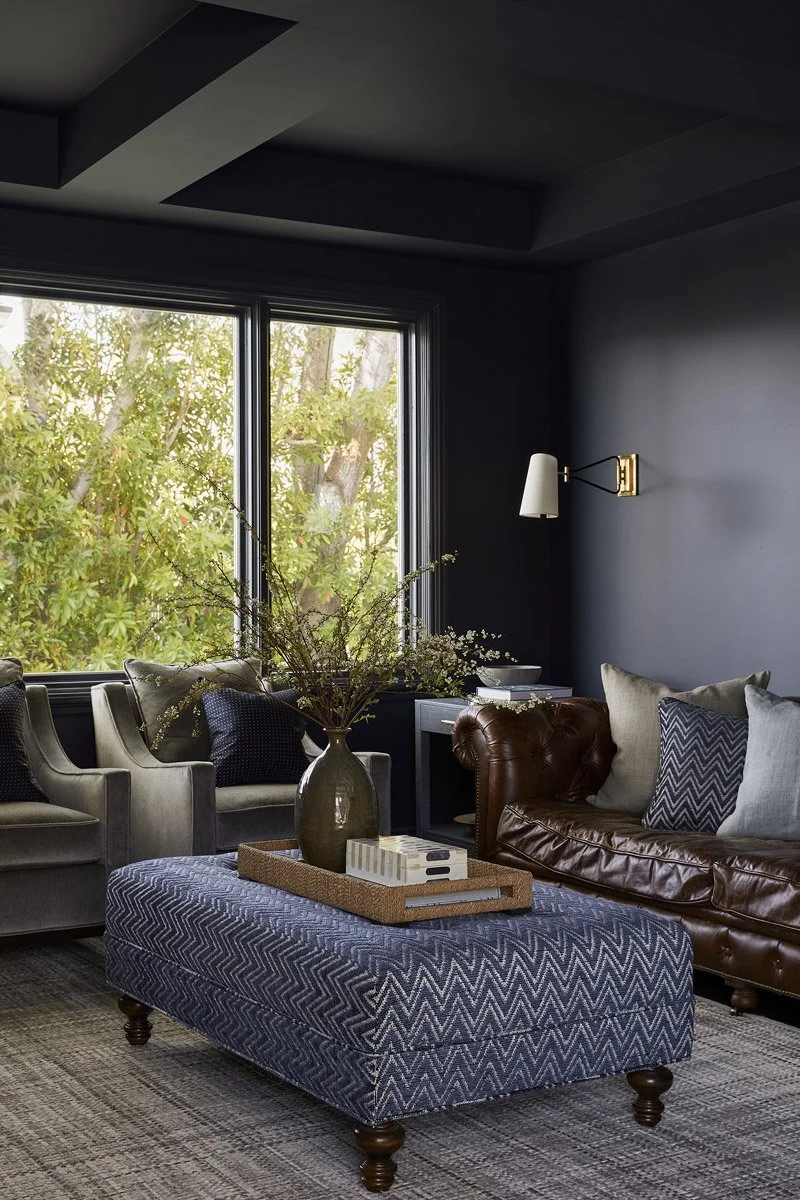 den with navy walls, leather sofa, upholstered ottoman and garden views