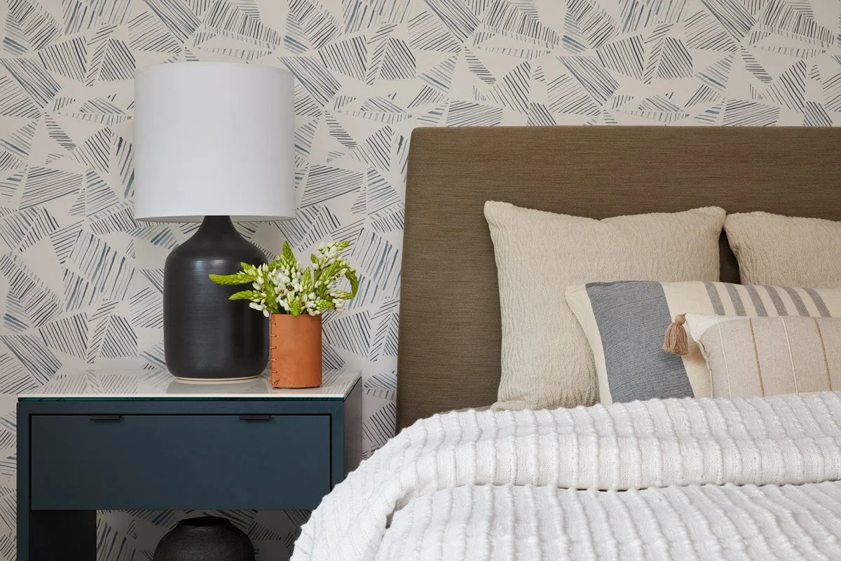 bedroom with leaf print wallpaper, upholstered headboard and navy nightstand