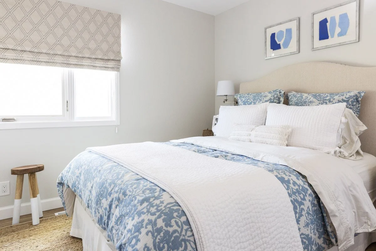 bedroom with blue and white bedding, roman shades and framed art