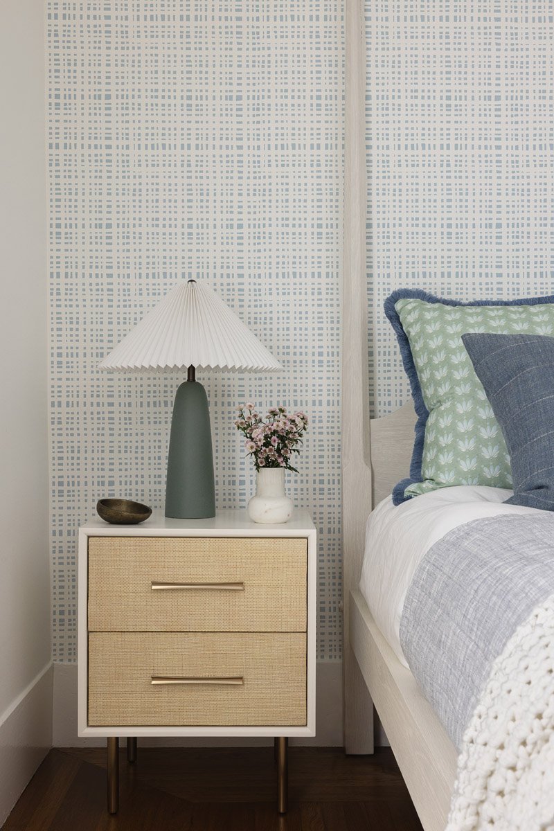 bedside table with sculptural lamp beside a grid patterned wallpaper