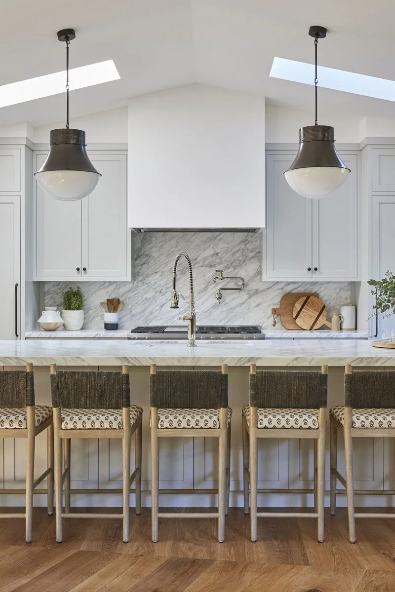 white kitchen with marble backsplash, plaster range hood and two pendant lights