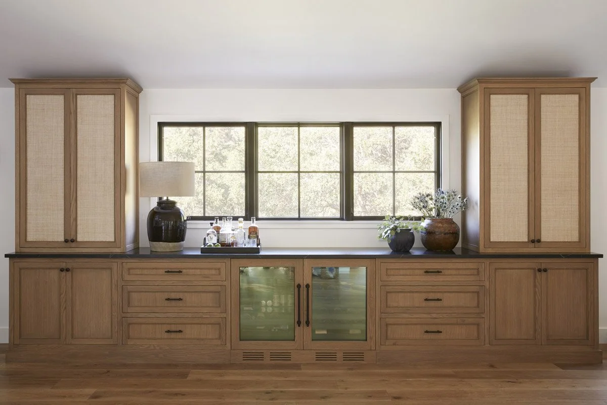 white oak built-in cabinetry with cane doors and beverage fridges under a window