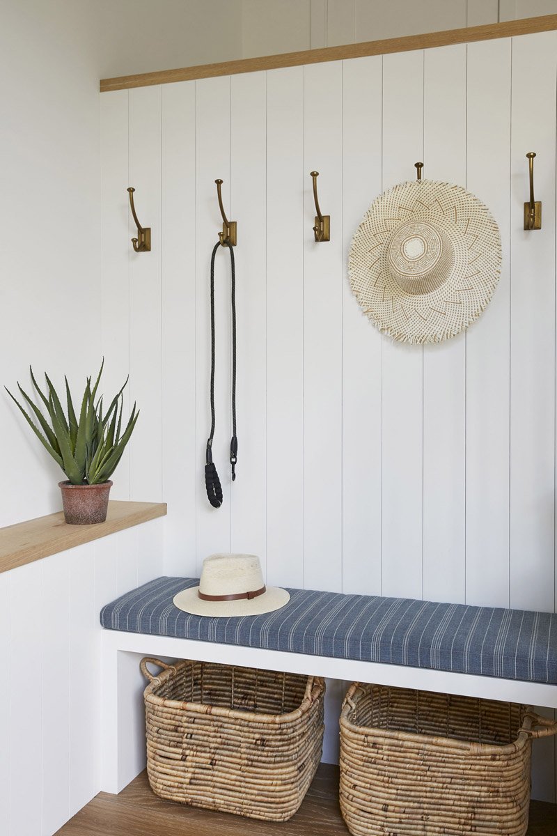 mudroom bench with woven baskets, wall hooks and white panelled walls