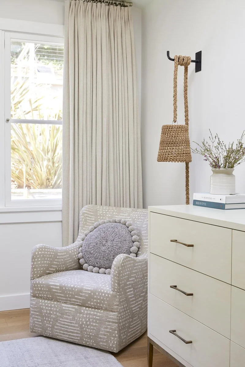 bedroom corner with upholstered swivel chair, white dresser and linen curtains