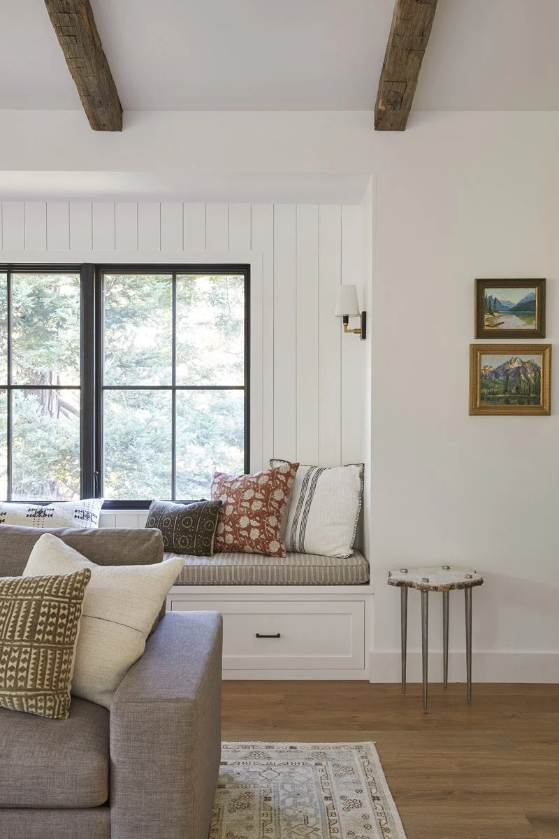 window seat with cushions beside a grey sofa under wood ceiling beams