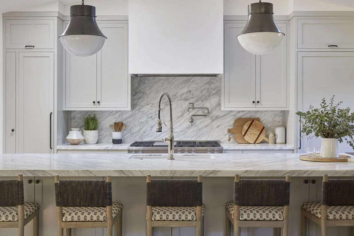 white kitchen with marble backsplash, oversized pendant lights and woven stools
