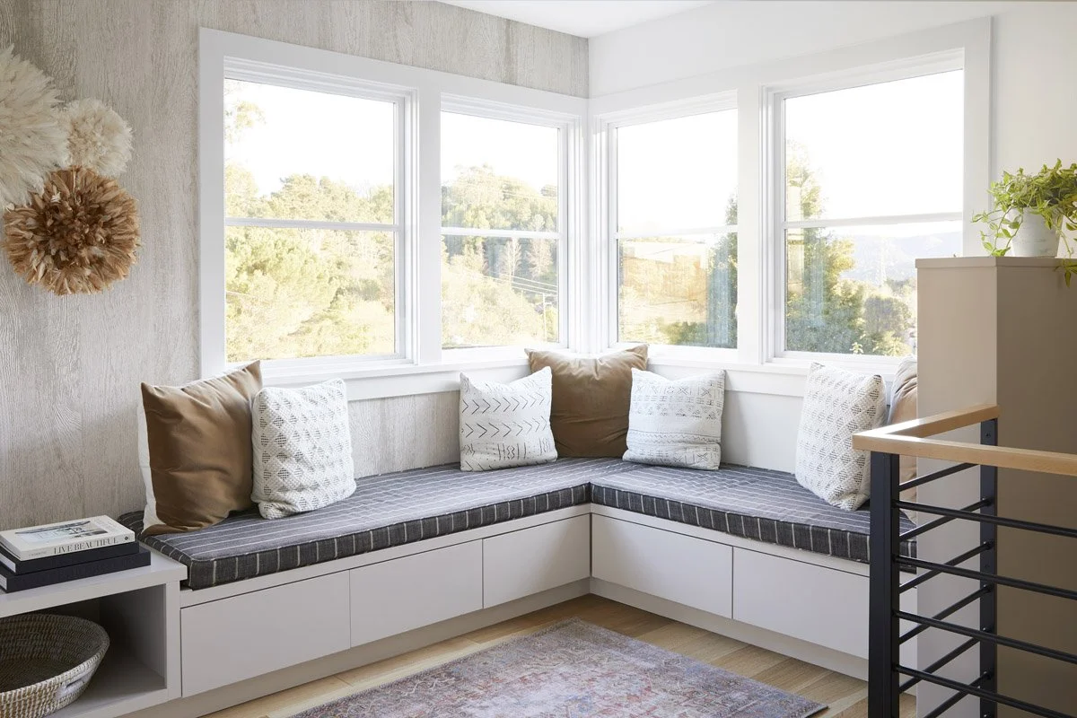 built-in corner banquette with cushions beneath a wall of windows