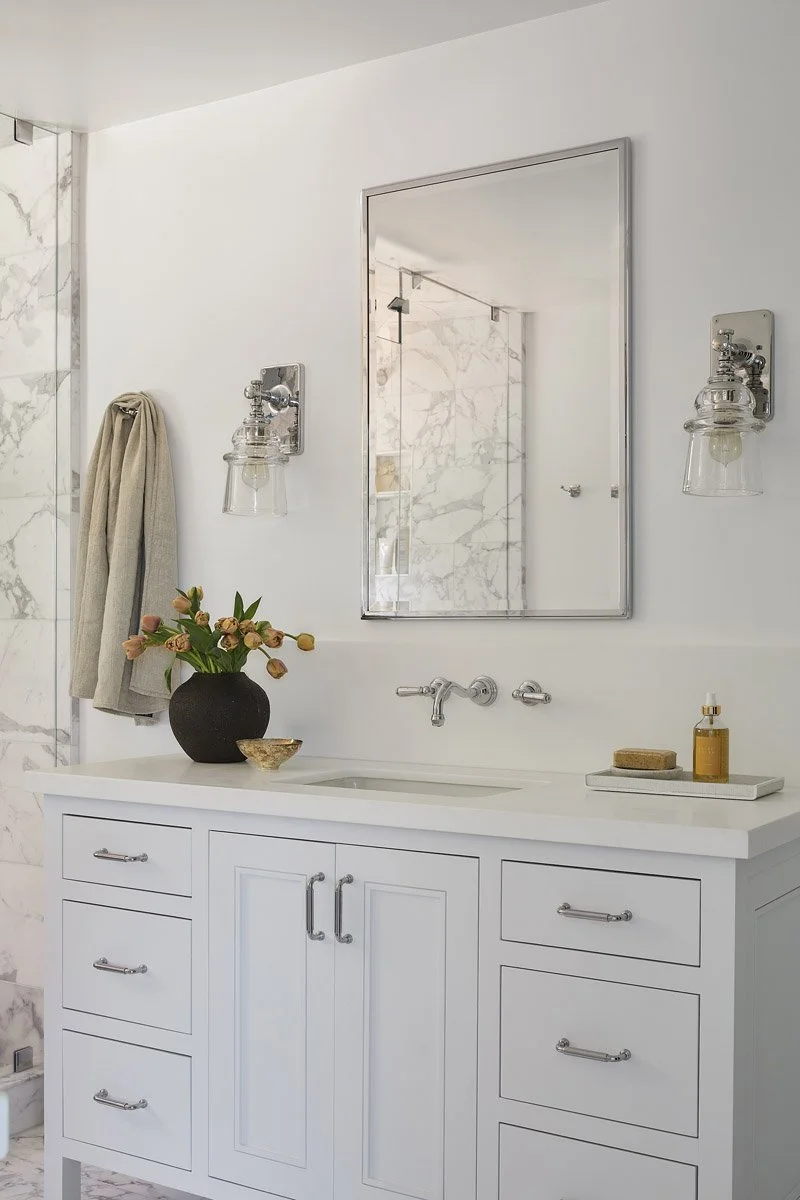 white bathroom vanity with marble backsplash and wall-mounted brass taps
