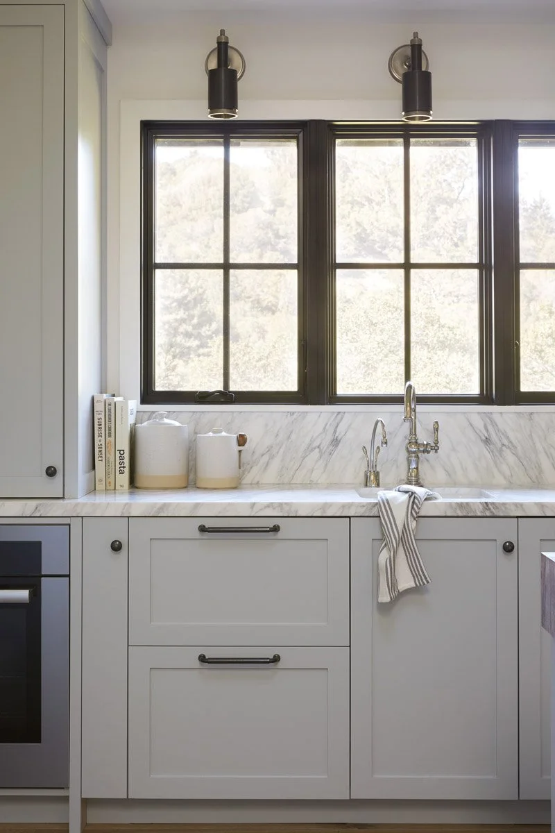 white kitchen cabinetry with black-framed window and marble backsplash
