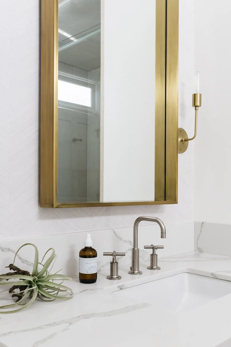 brass framed mirror and sconce above a marble vanity