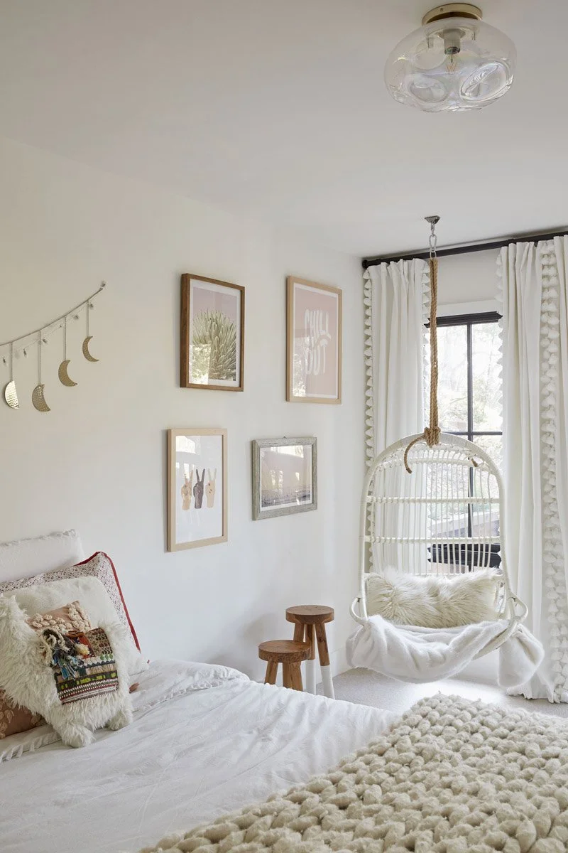 girls bedroom with framed artwork, hanging rattan chair and knit blanket