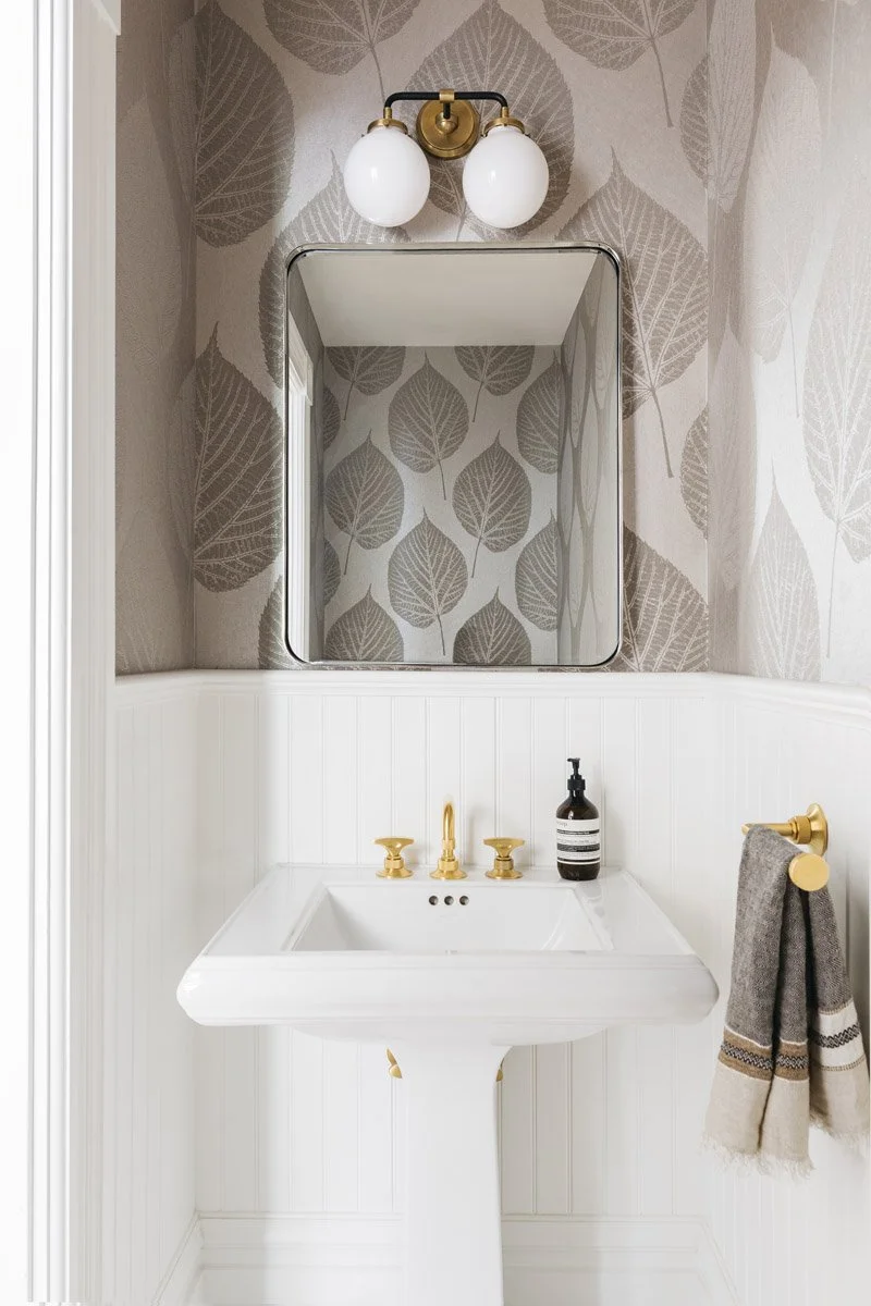 powder room with leaf print wallpaper, pedestal sink and brass taps