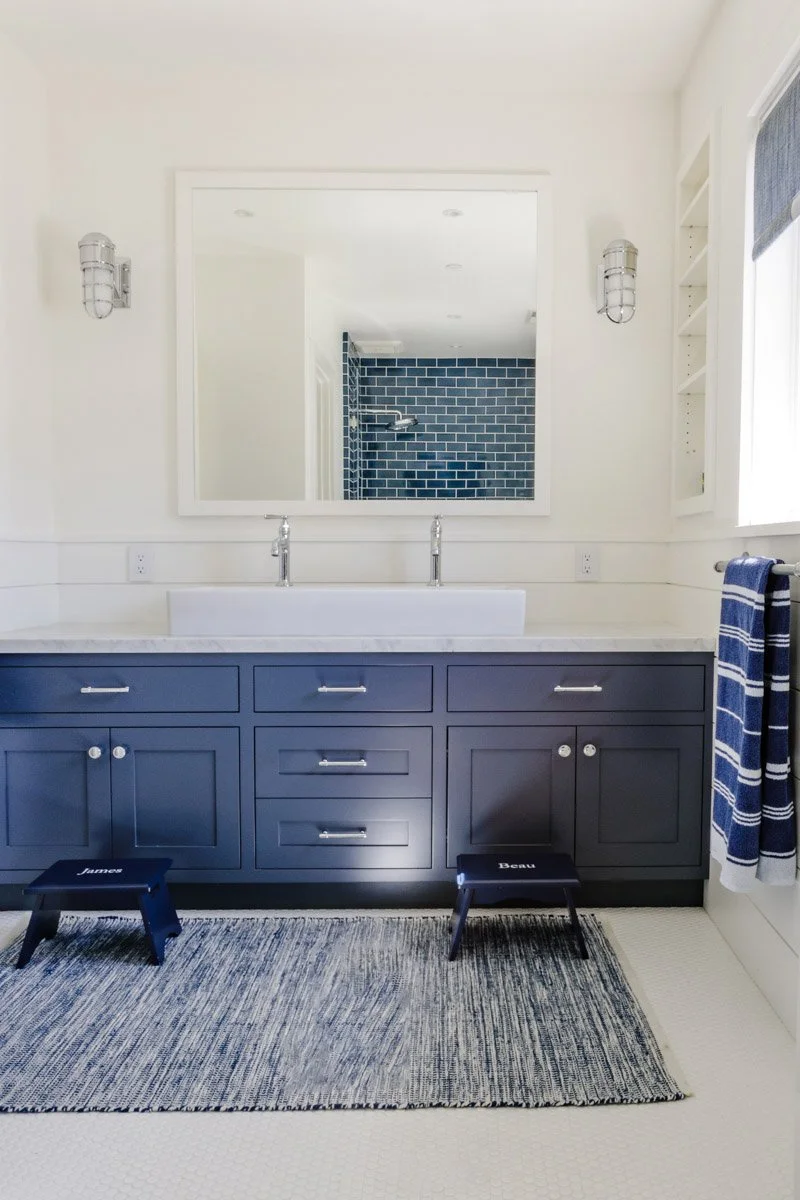 bathroom with navy double vanity, white walls and woven rug